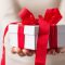 Pessoa segurando uma caixa de presente branca com laço vermelho, representando presentes de fim de ano para clientes.