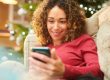 Mulher lendo uma mensagem no celular em clima de Natal, representando uma mensagem de natal para empresas enviada de forma humanizada.