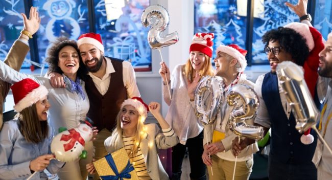 festa-de-final-de-ano-na-empresa-colaboradores-comemorando-baloes Grupo de colegas celebrando a festa de final de ano na empresa com gorros natalinos, balões festivos e clima descontraído.