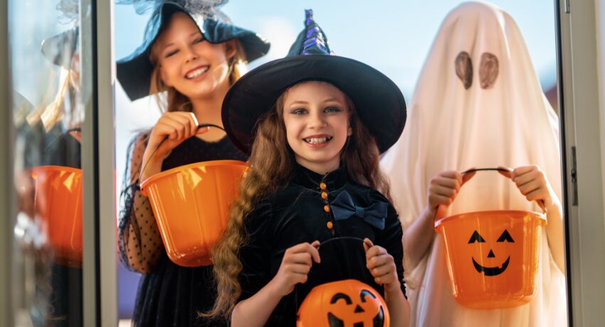 Halloween 2026 — Ações criativas e temáticas para encantar o público. Crianças fantasiadas de bruxa e fantasma segurando baldes de Halloween.