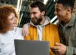 Três colegas de trabalho sorrindo em frente a um notebook durante processo de onboarding nas empresas.