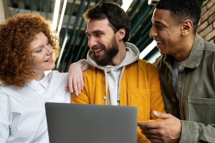 Três colegas de trabalho sorrindo em frente a um notebook durante processo de onboarding nas empresas.