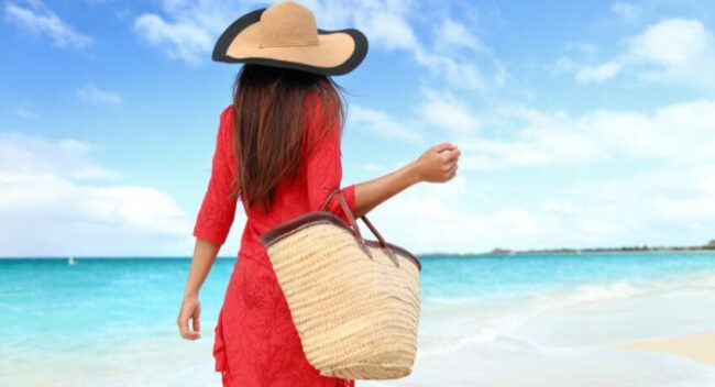 Mulher com bolsa de palha caminhando na praia representando o estilo de vida litorâneo sofisticado