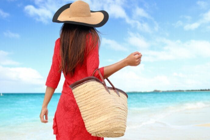 Mulher com bolsa de palha caminhando na praia representando o estilo de vida litorâneo sofisticado