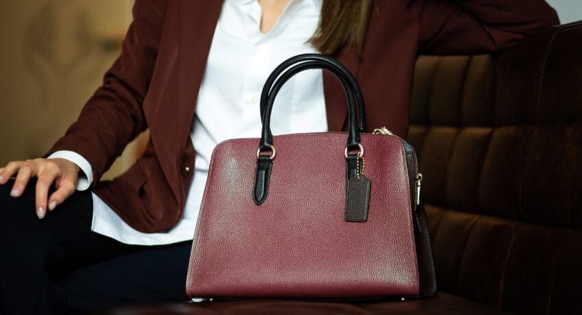 Bolsas que atravessam tendências e constroem identidade Bolsa estruturada elegante em tom vinho apoiada em sofá, representando estilo atemporal e sofisticação