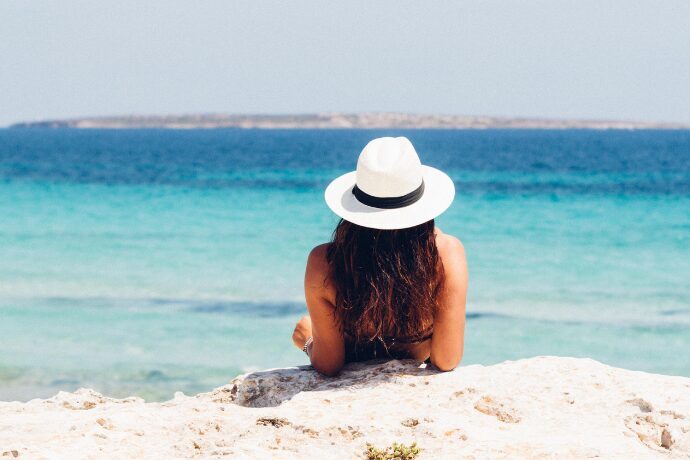 Mulher com chapéu observando o mar em cenário paradisíaco que representa estilo de vida litorâneo e luxo
