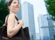 Mulher caminhando em cenário urbano sofisticado com bolsa elegante e prédios modernos ao fundo