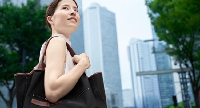 Mulher caminhando em cenário urbano sofisticado com bolsa elegante e prédios modernos ao fundo