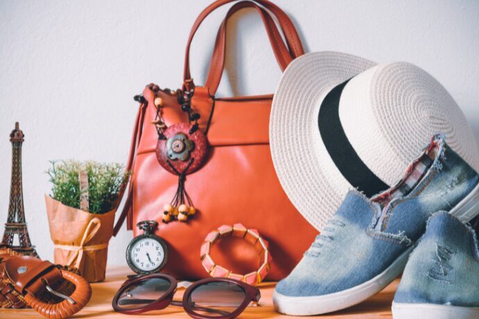 Bolsa de couro laranja com chapéu, óculos de sol e calçados casuais organizados sobre mesa, representando planejamento de viagem sofisticada para Orlando.