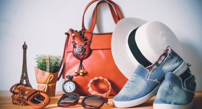 Bolsa de couro laranja com chapéu, óculos de sol e calçados casuais organizados sobre mesa, representando planejamento de viagem sofisticada para Orlando.