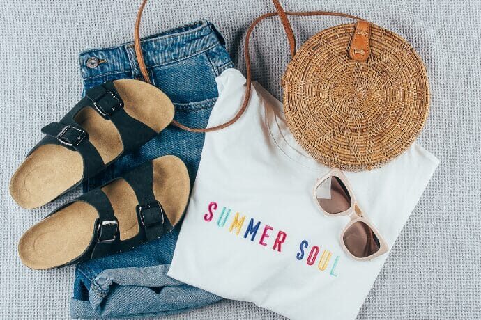 Composição de look de verão com bolsa de palha redonda, sandálias confortáveis, jeans e camiseta branca, representando estilo casual chic e lifestyle de luxo em Miami.