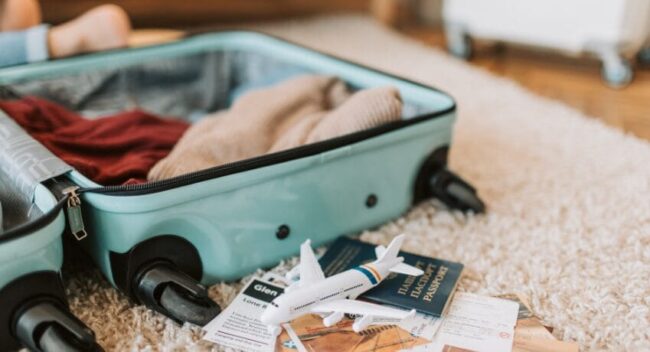 Mala de viagem aberta com roupas organizadas, passaportes e miniatura de avião, representando planejamento de fim de semana no campo com estilo.